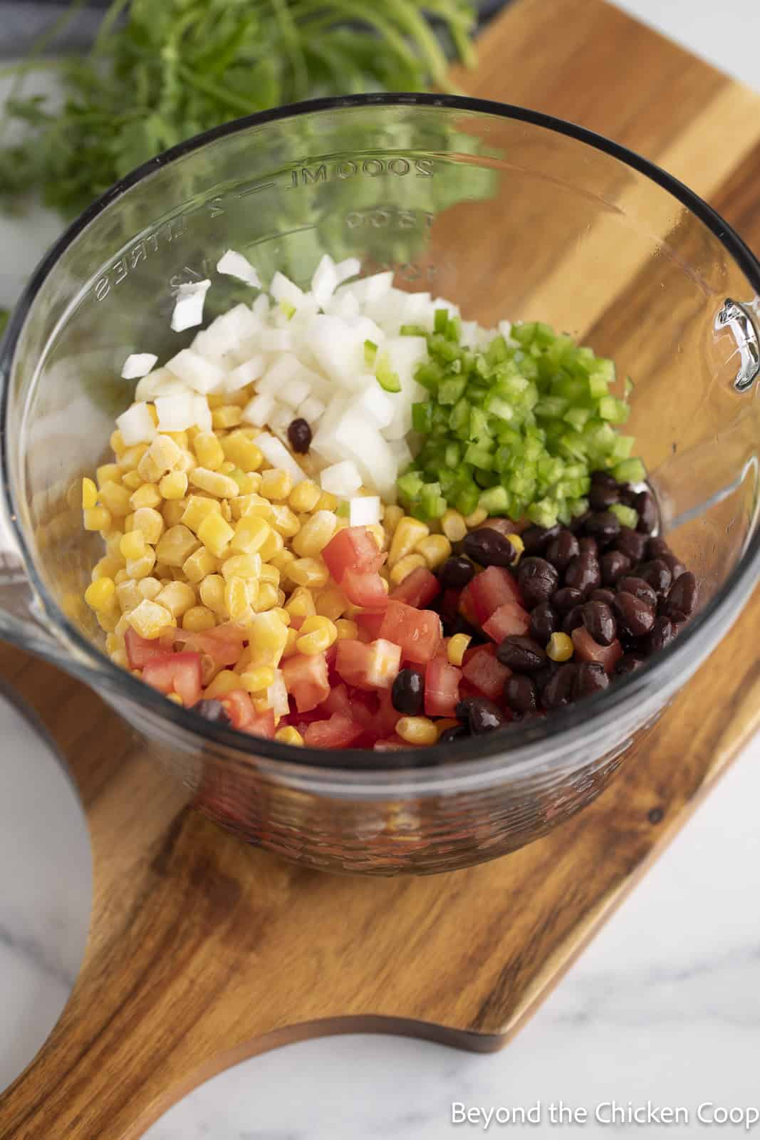 A glass bowl filled with black beans, corn, tomatoes, onions, and cilantro.