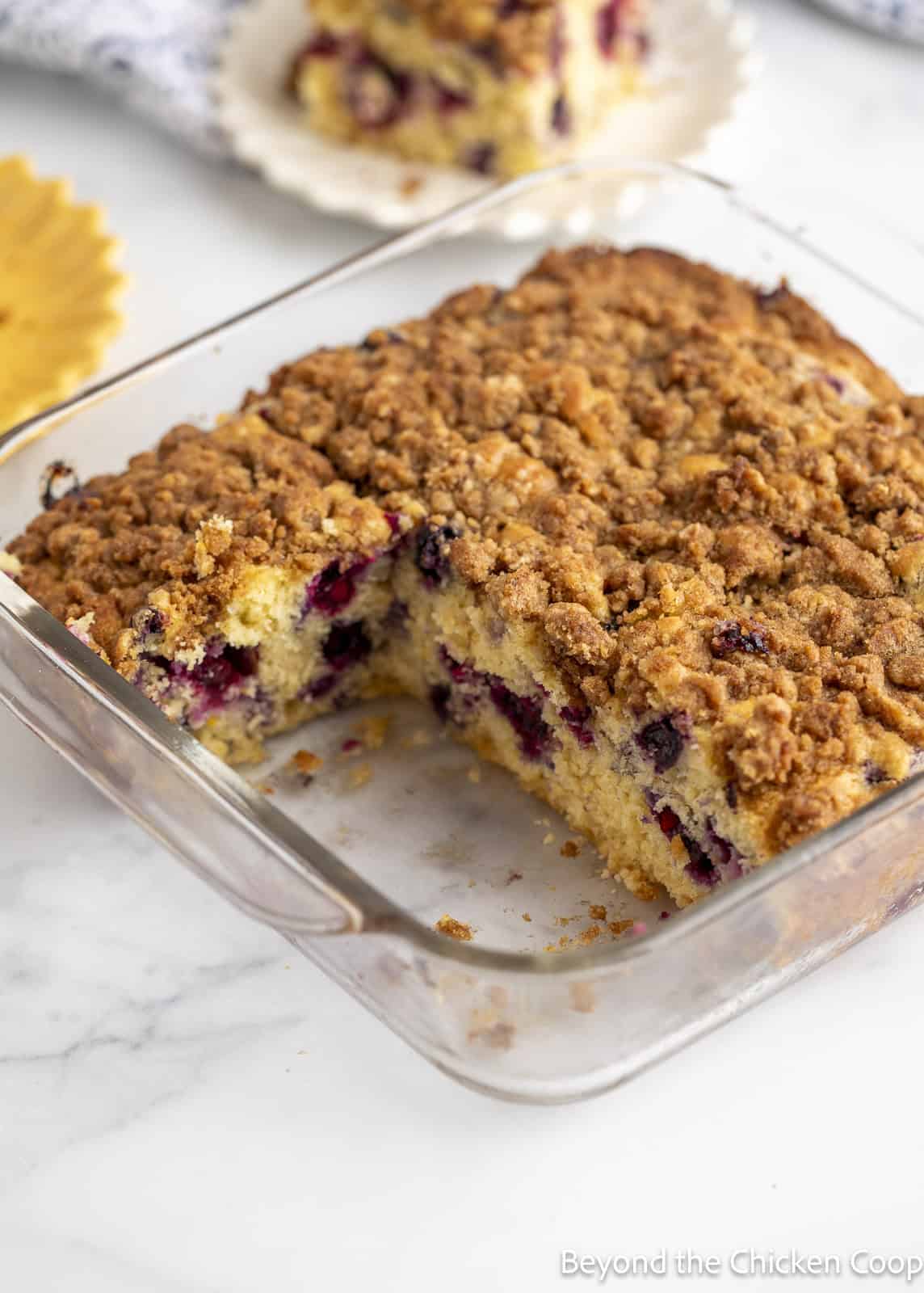 A coffee cake with blueberries and a crumb topping in a glass baking dish. 