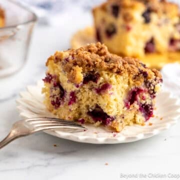 A slice of Blueberry Coffee Cake on a white plate with a fork next to the cake.