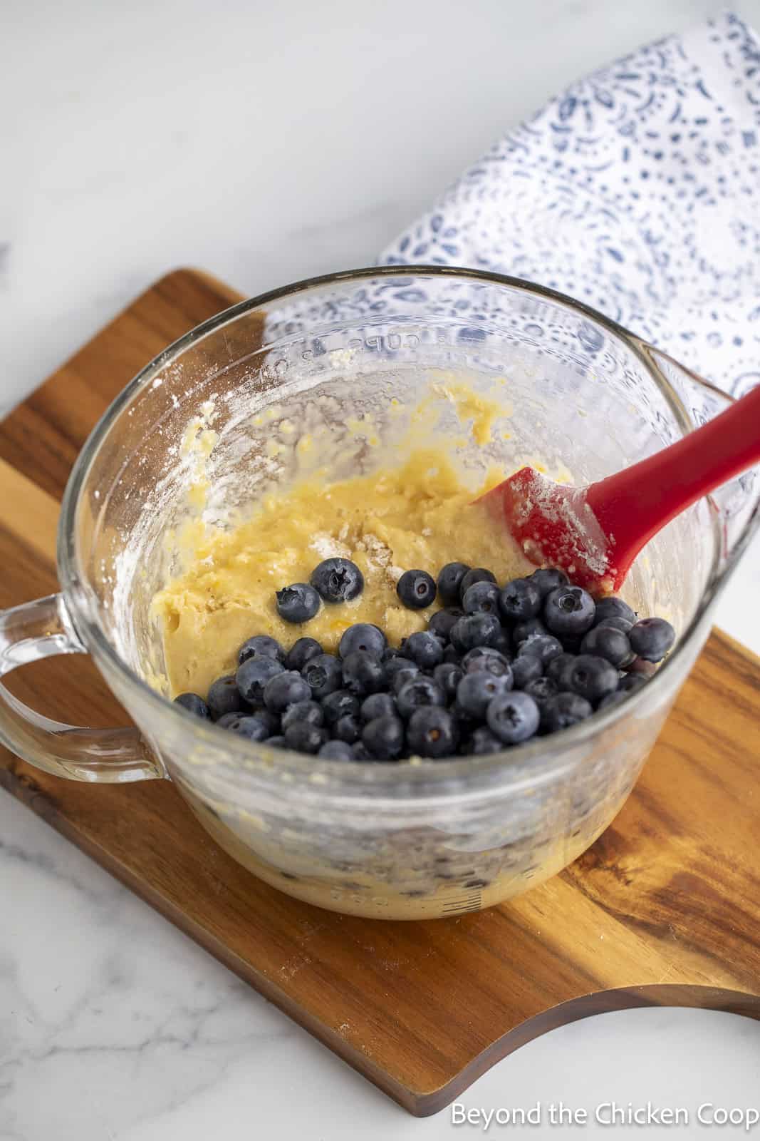 Cake batter with fresh blueberries on top in a glass mixing bowl. 
