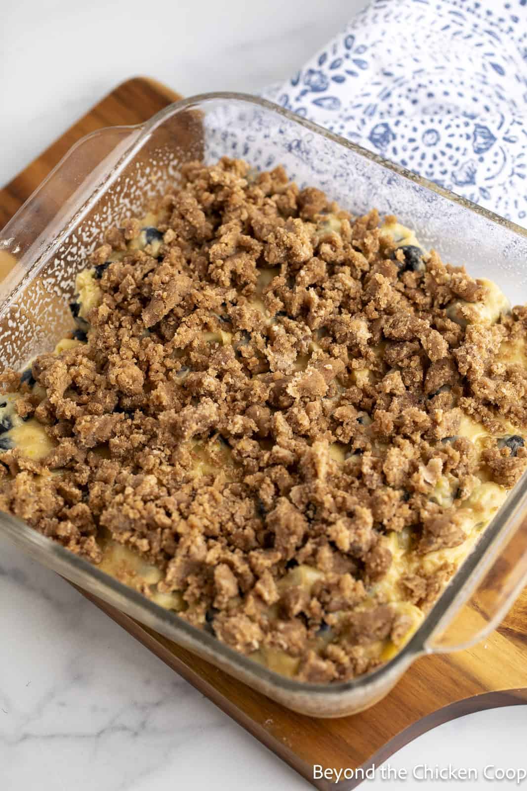An unbaked blueberry cake with a crumb topping in a glass cake pan. 