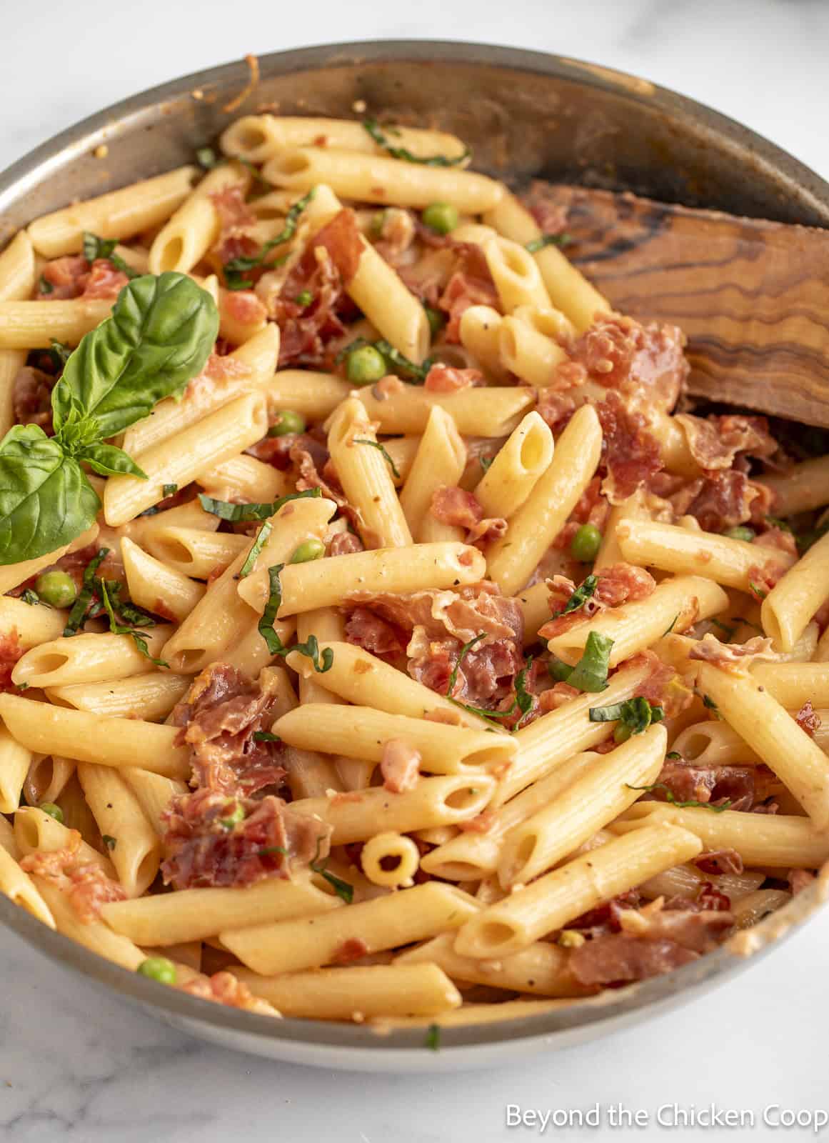 Pasta, prosciutto, peas, and fresh basil in a skillet. 