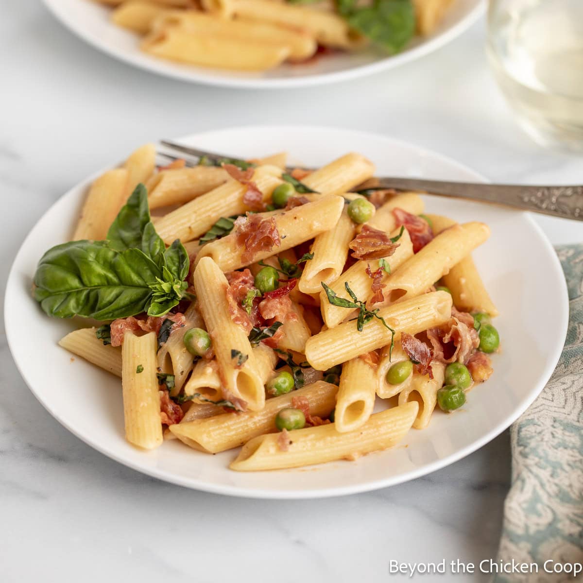 A plate filled with pasta with prosciutto and peas. 