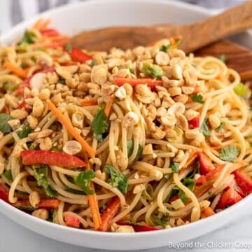 Asian Noodle Salad in a white bowl with a wooden spoon.