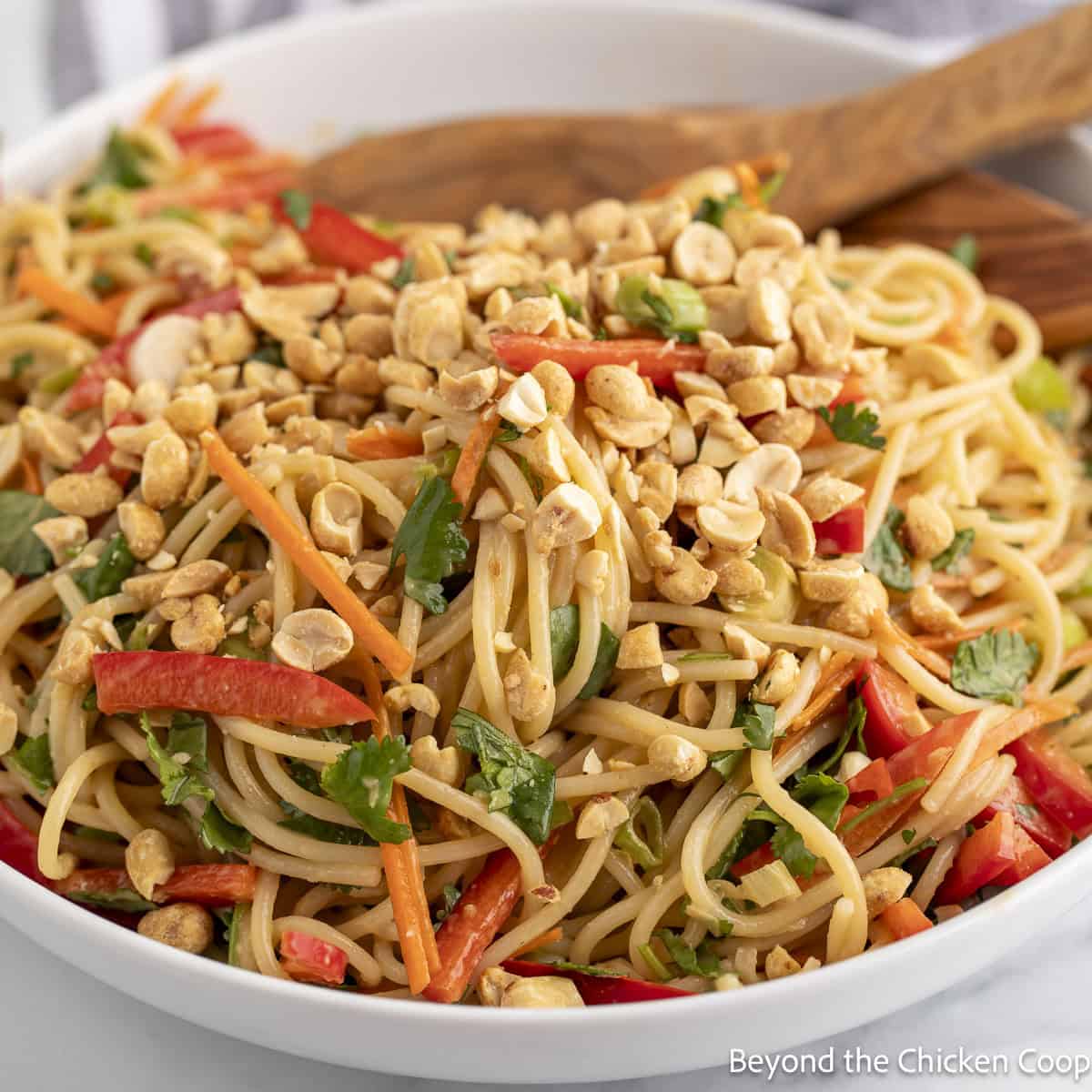 Asian Noodle Salad in a white bowl with a wooden spoon. 