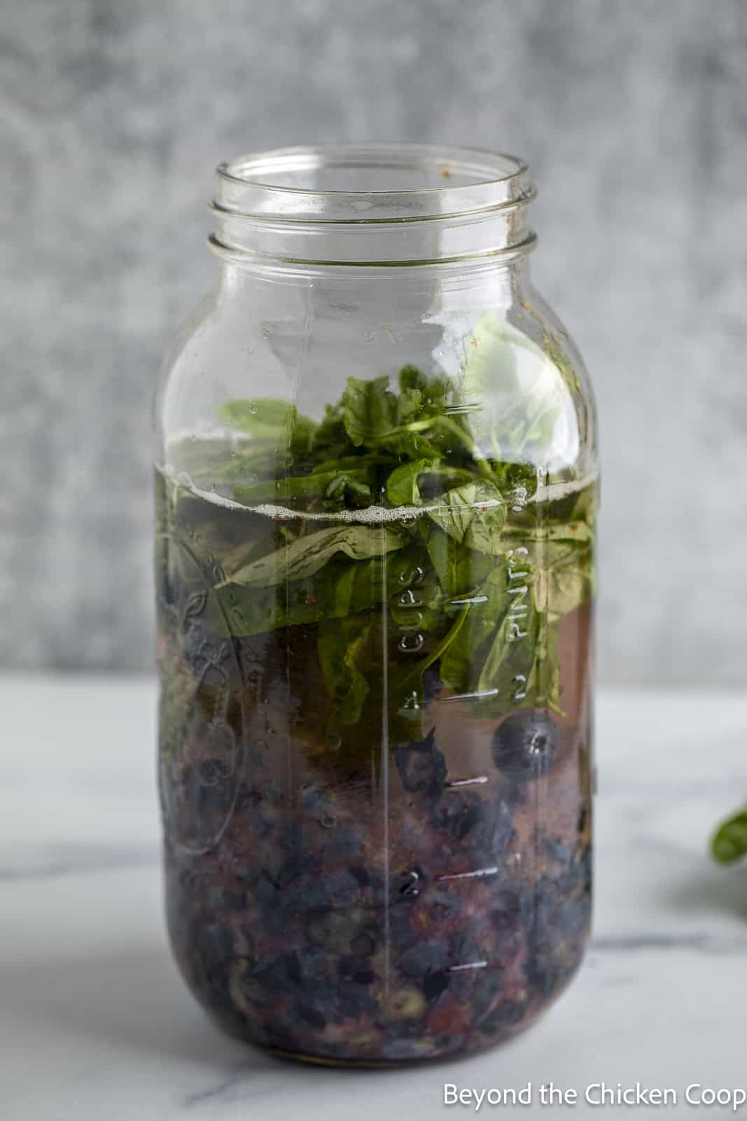 Basil added to a jar with vinegar and berries. 