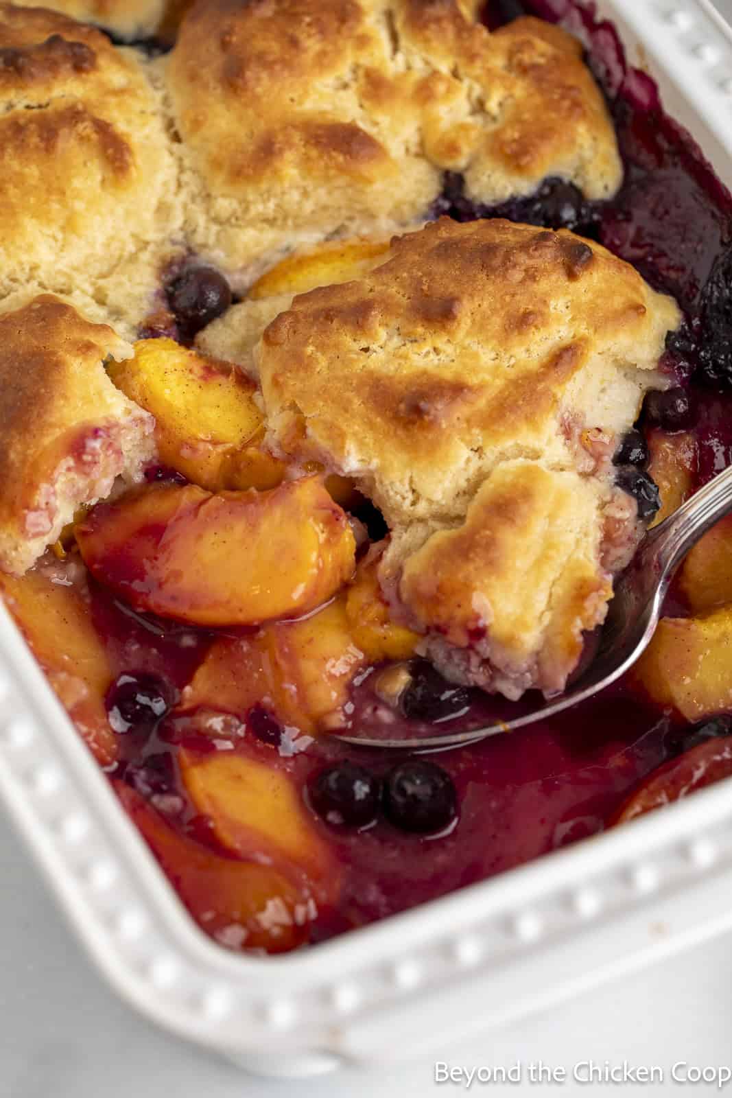 Peach cobbler with blueberries in a white dish.