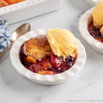 Blueberry Peach Cobbler with a scoop of vanilla ice cream in a white dish.