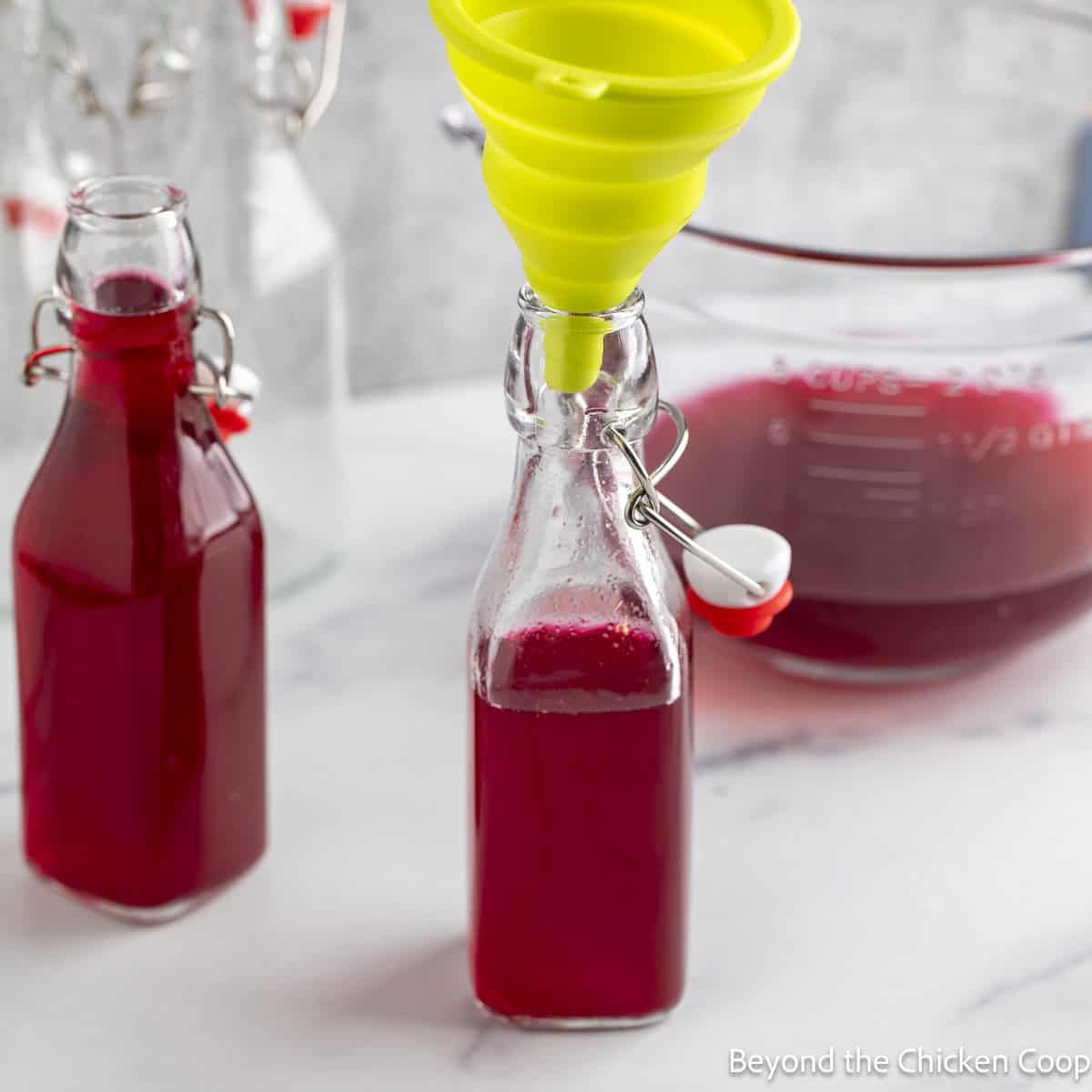 Small glass bottles being filled with a red colored vinegar. 