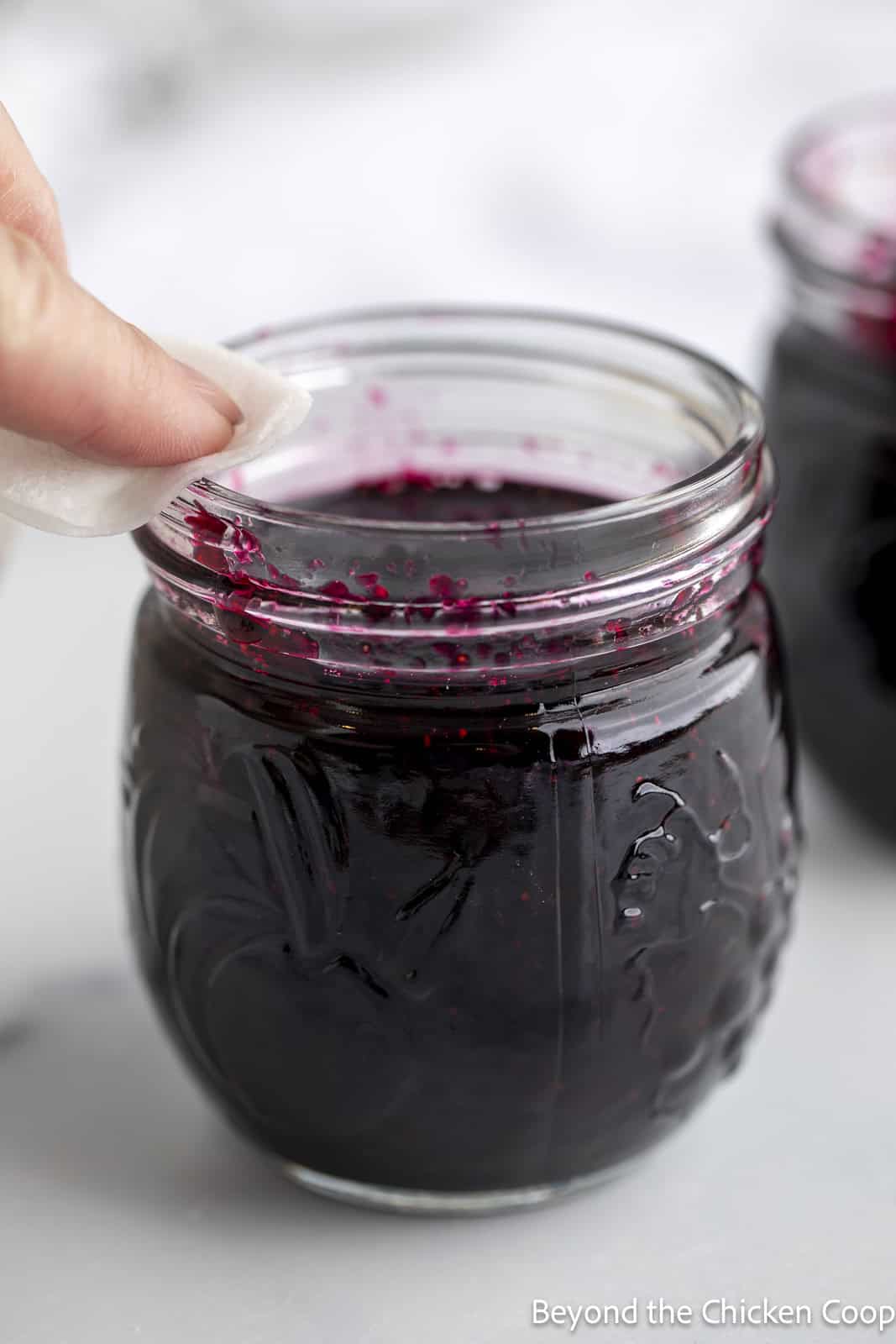 Wiping down the rim of a small canning jar filled with jam. 