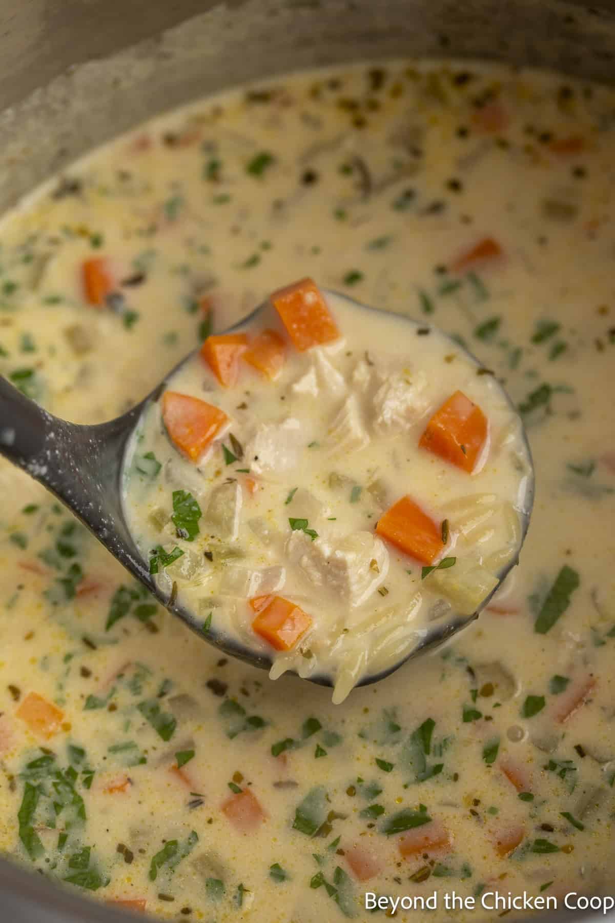 Creamy chicken soup in a pot with a black ladle.