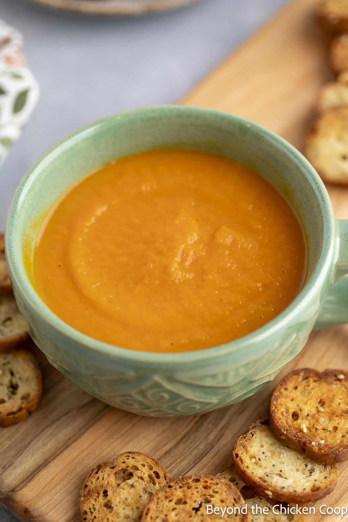 Carrot soup in a green bowl next to round crackers.