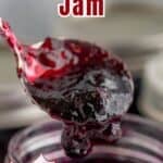A spoonful of jam dripping off of the spoon into a jar.