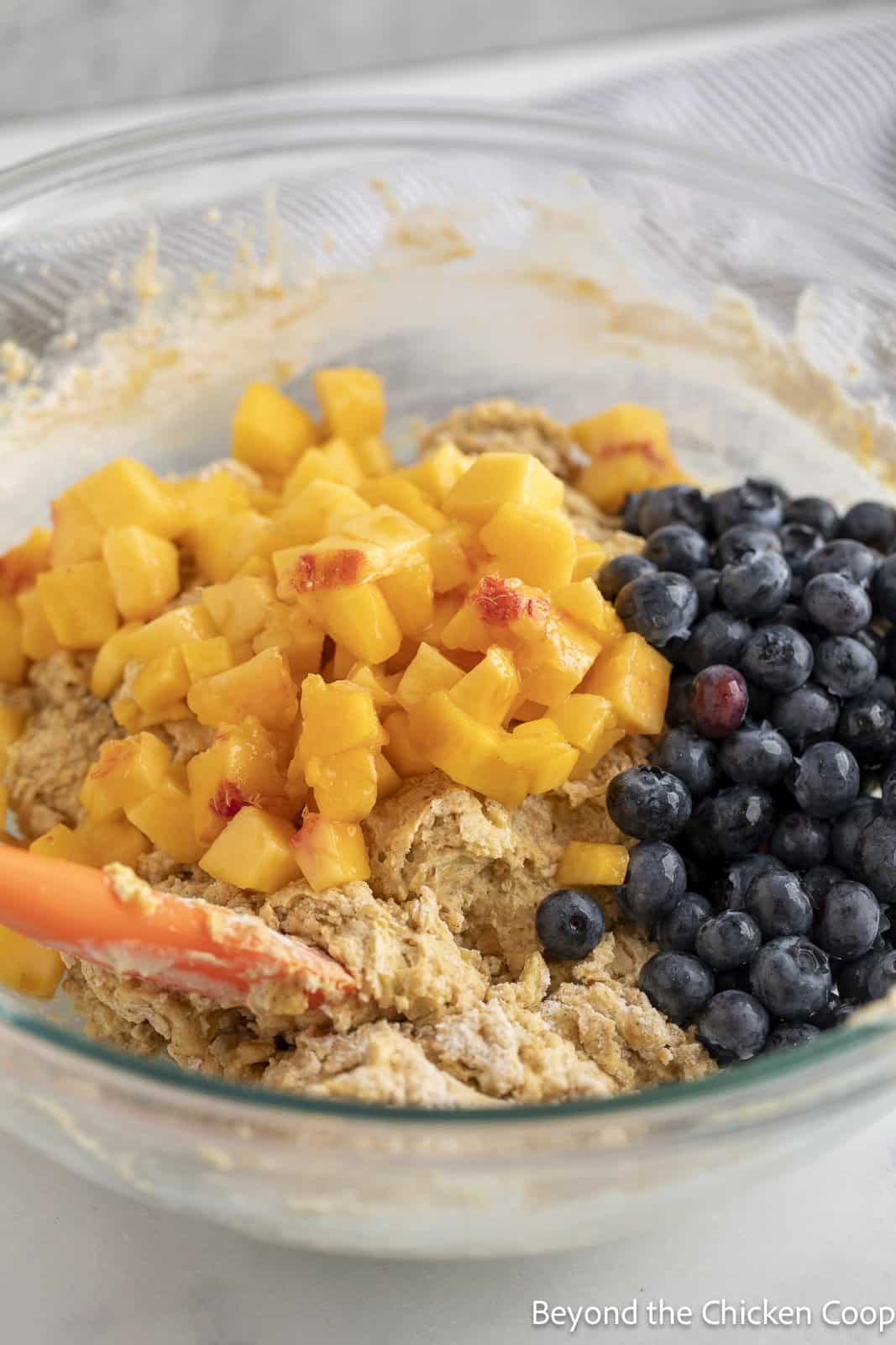 Chopped peaches and blueberries in a bowl with muffin batter.