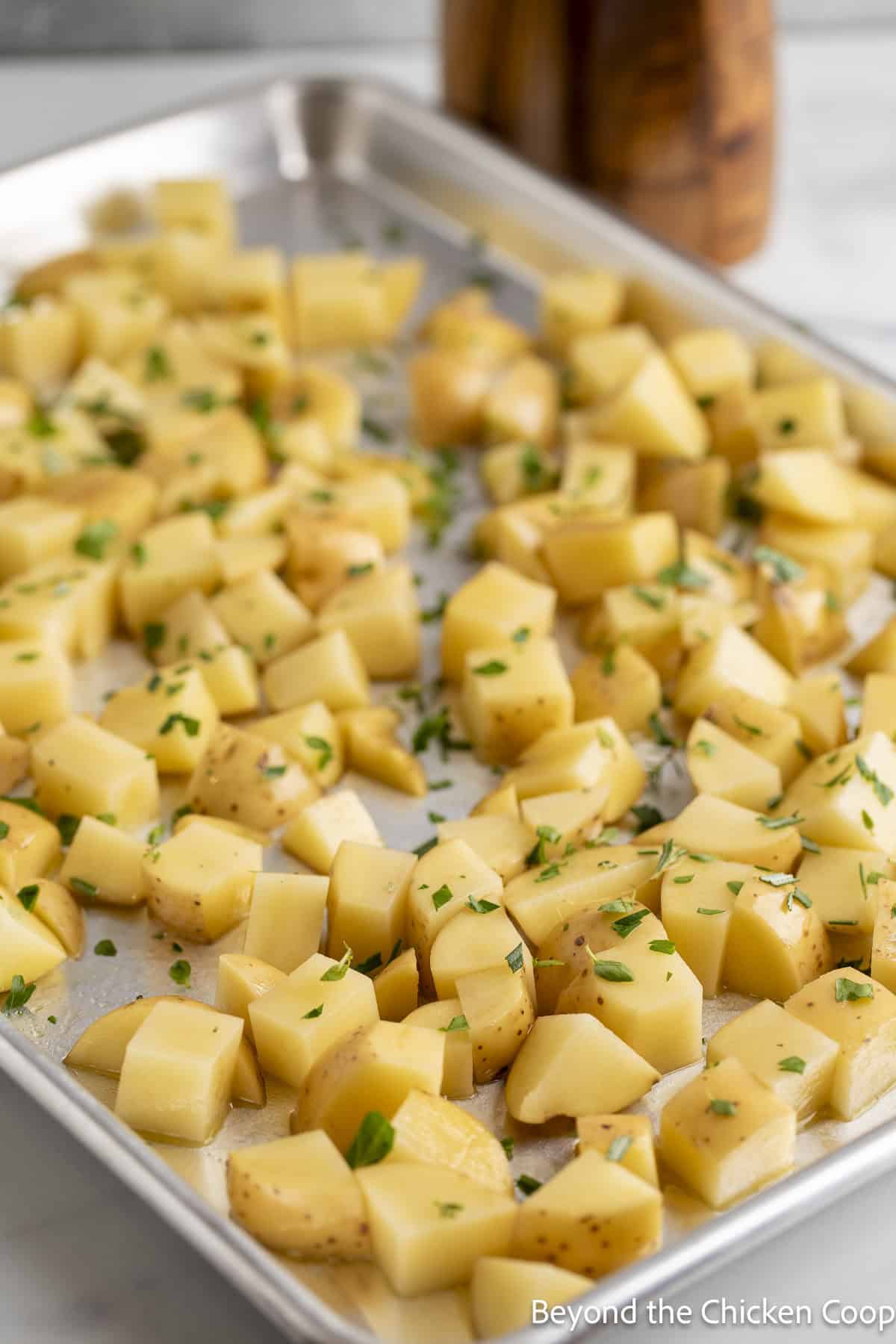 Cubed potatoes with fresh herbs on a baking sheet.
