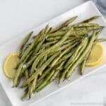 Oven Roasted Green Beans on a white platter with lemon slices.