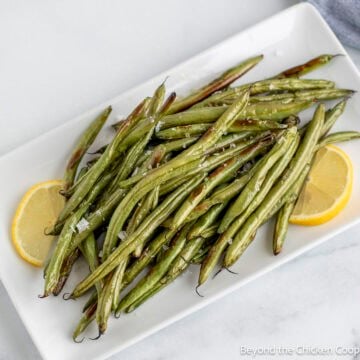 Oven Roasted Green Beans on a white platter with lemon slices.