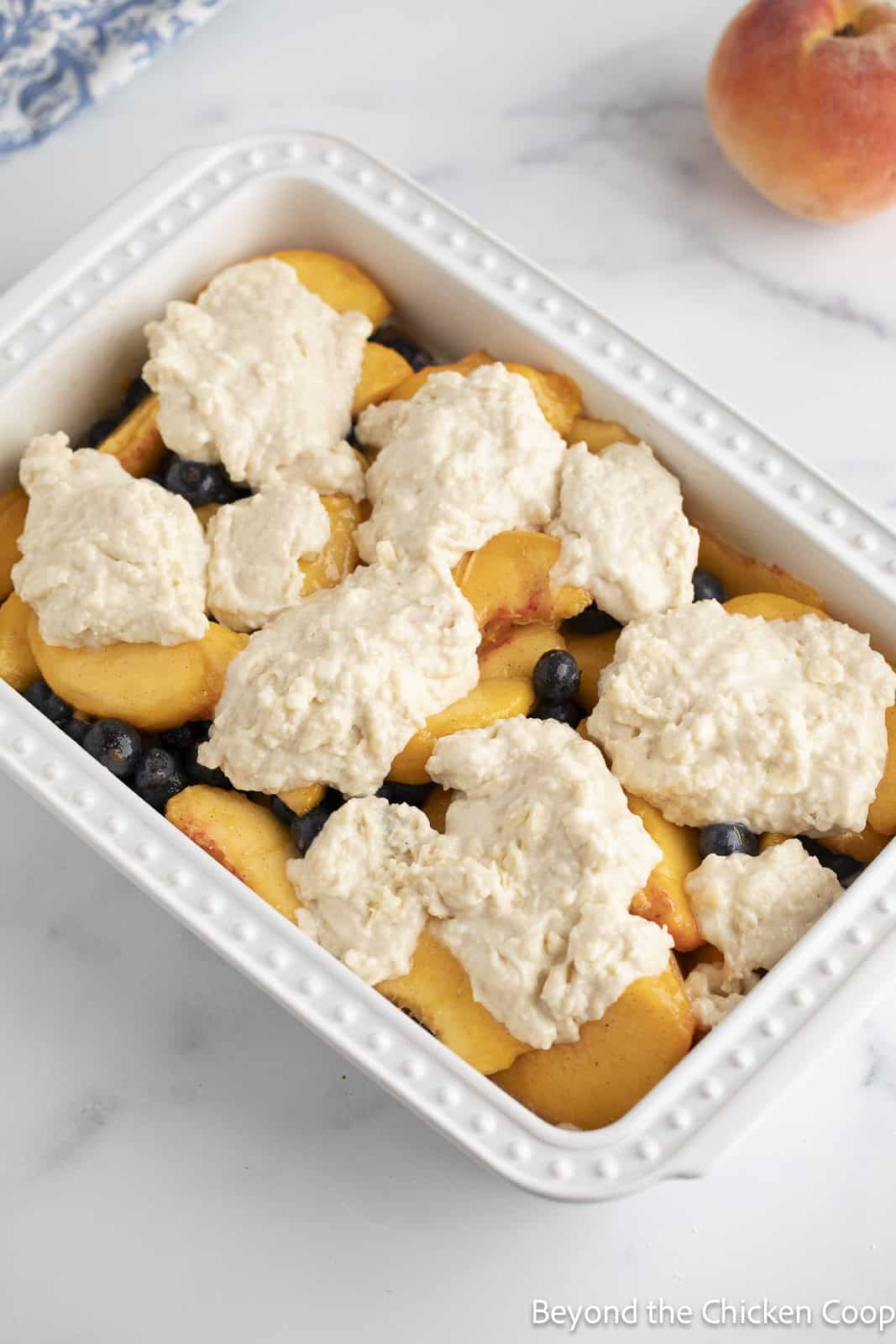 Dollops of cobbler batter on top of a layer of fruit. 