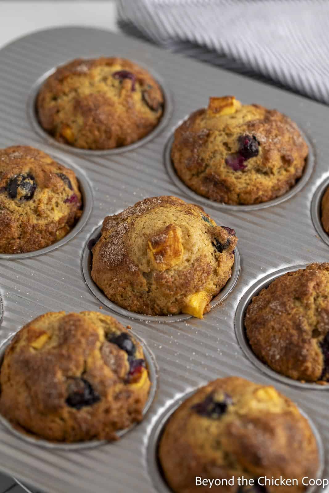Baked blueberry peach muffins in a muffin tin.
