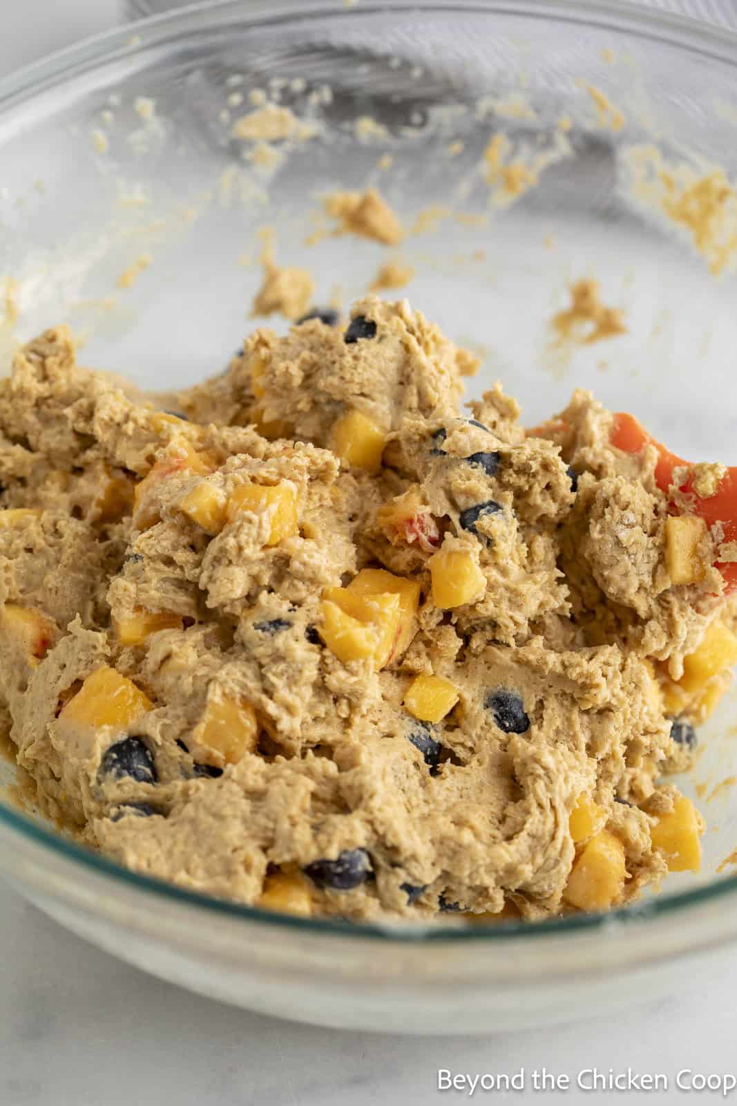 Muffin batter with chunks of peaches and blueberries in a glass bowl.
