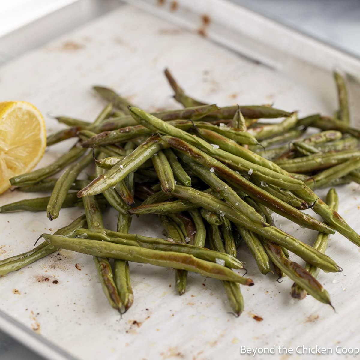 Roasted beans on a baking sheet with a half of a lemon.