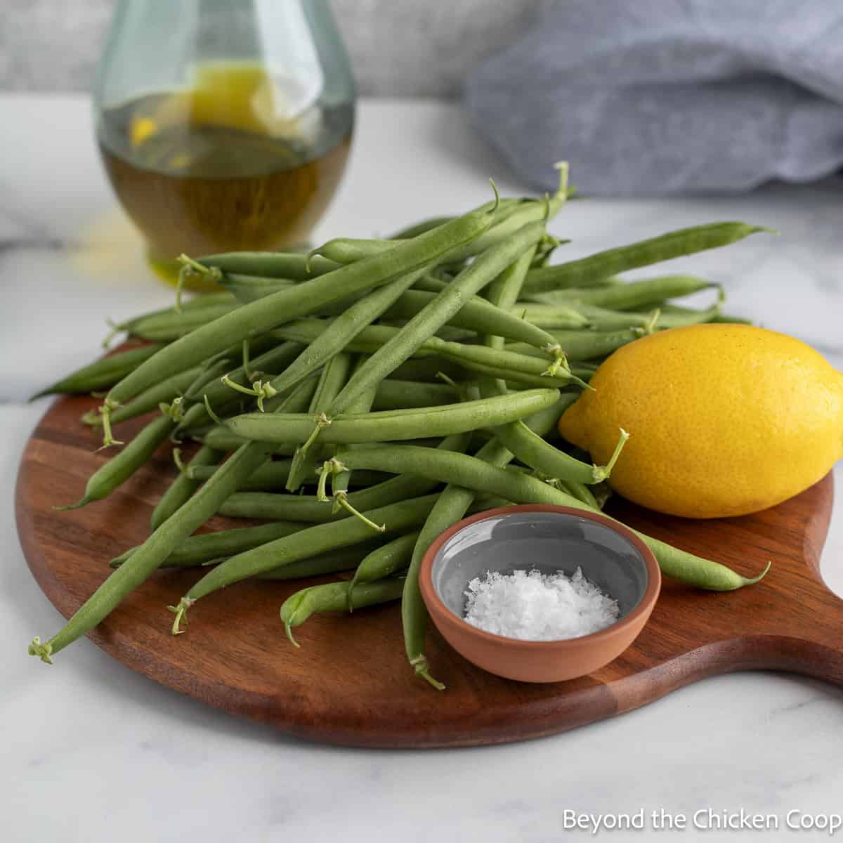 Fresh green beans on a board with a fresh lemon and a small bowl of salt. 