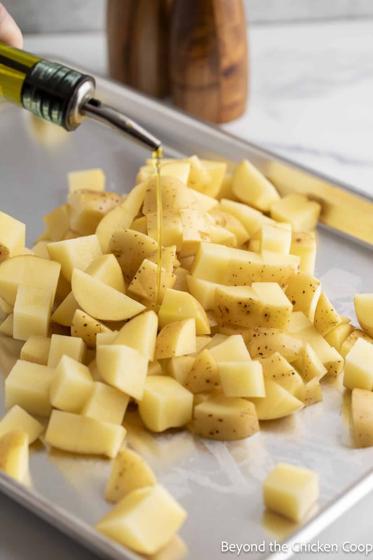 Pouring olive oil over potatoes on a baking sheet.