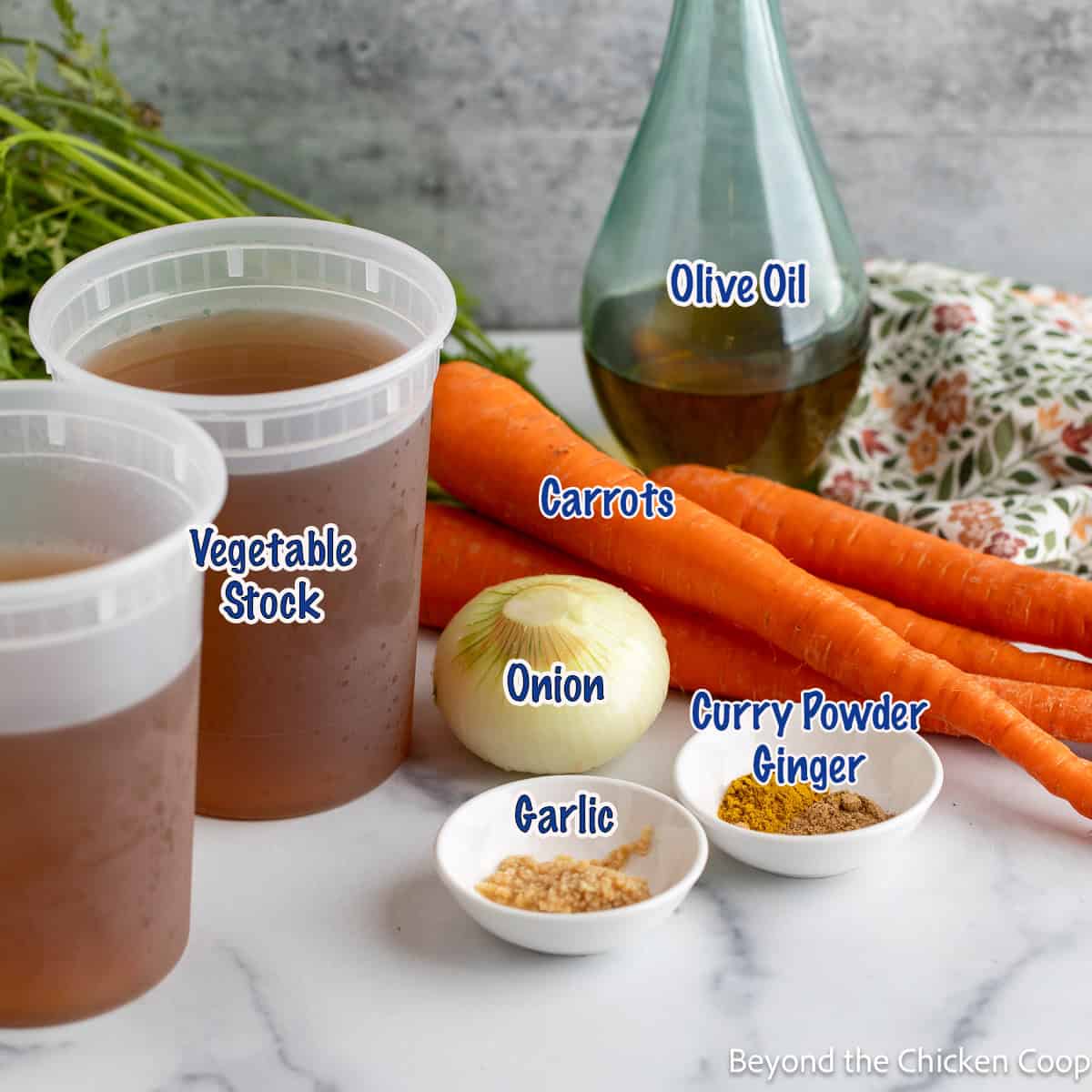 Carrots, veggie stock, an onion, ginger powder, and curry powder on a white counter.