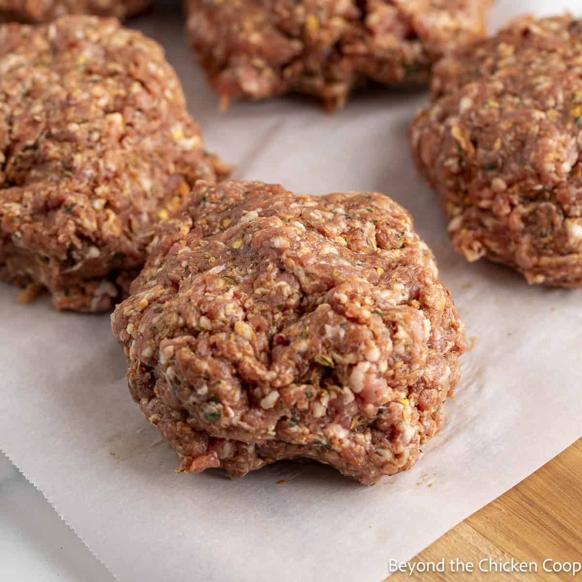 Patties of uncooked Italian sausage on parchment paper. 