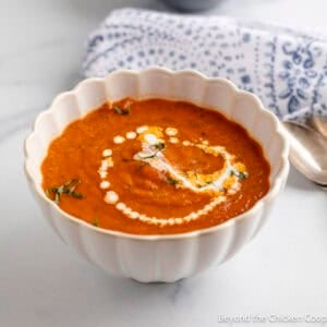 A bowl of Tomato Basil Soup with fresh basil on top and a swirl of cream.