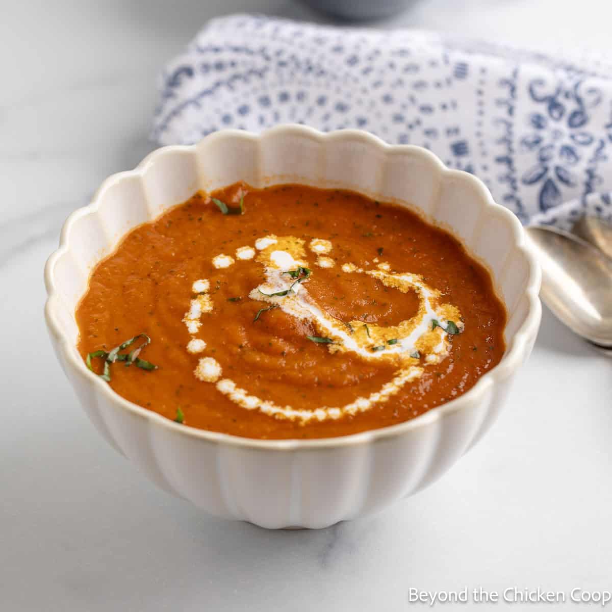A bowl of Tomato Basil Soup with fresh basil on top and a swirl of cream.