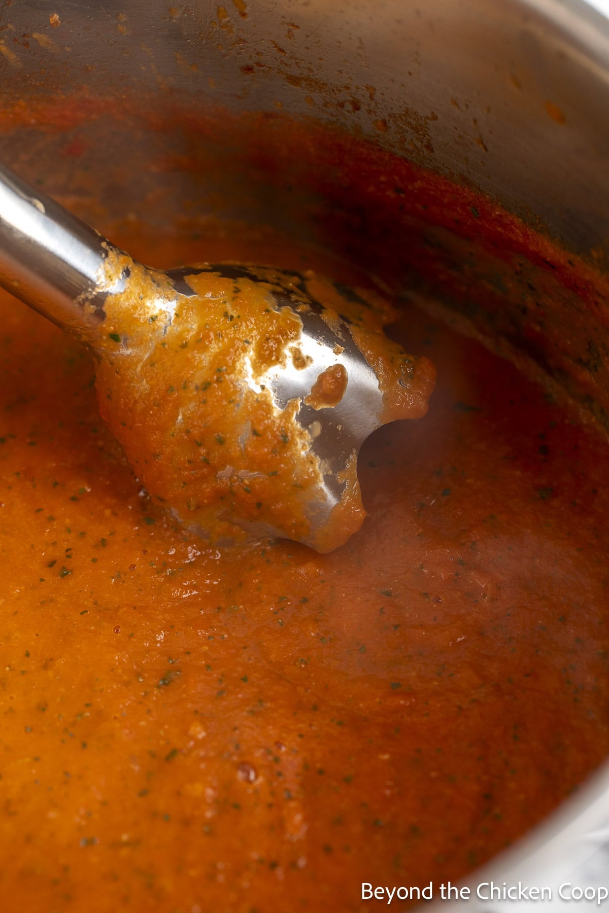 An immersion mixer in a pot of tomato soup. 