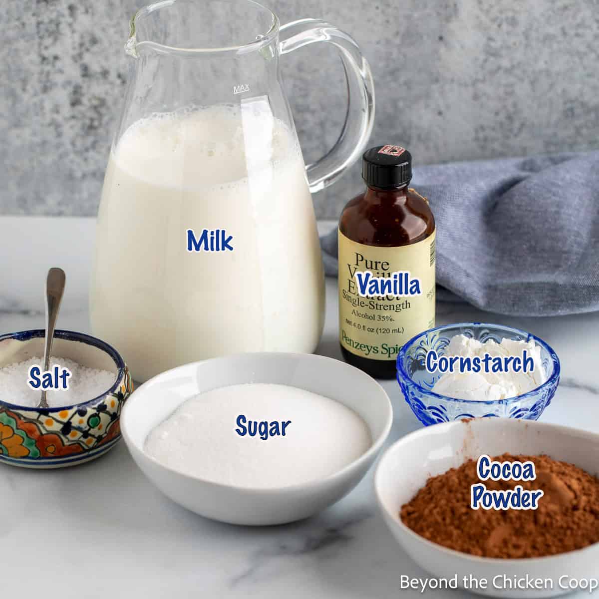 A pitcher with milk, and a few bowls filled with sugar, cocoa powder, and cornstarch. 