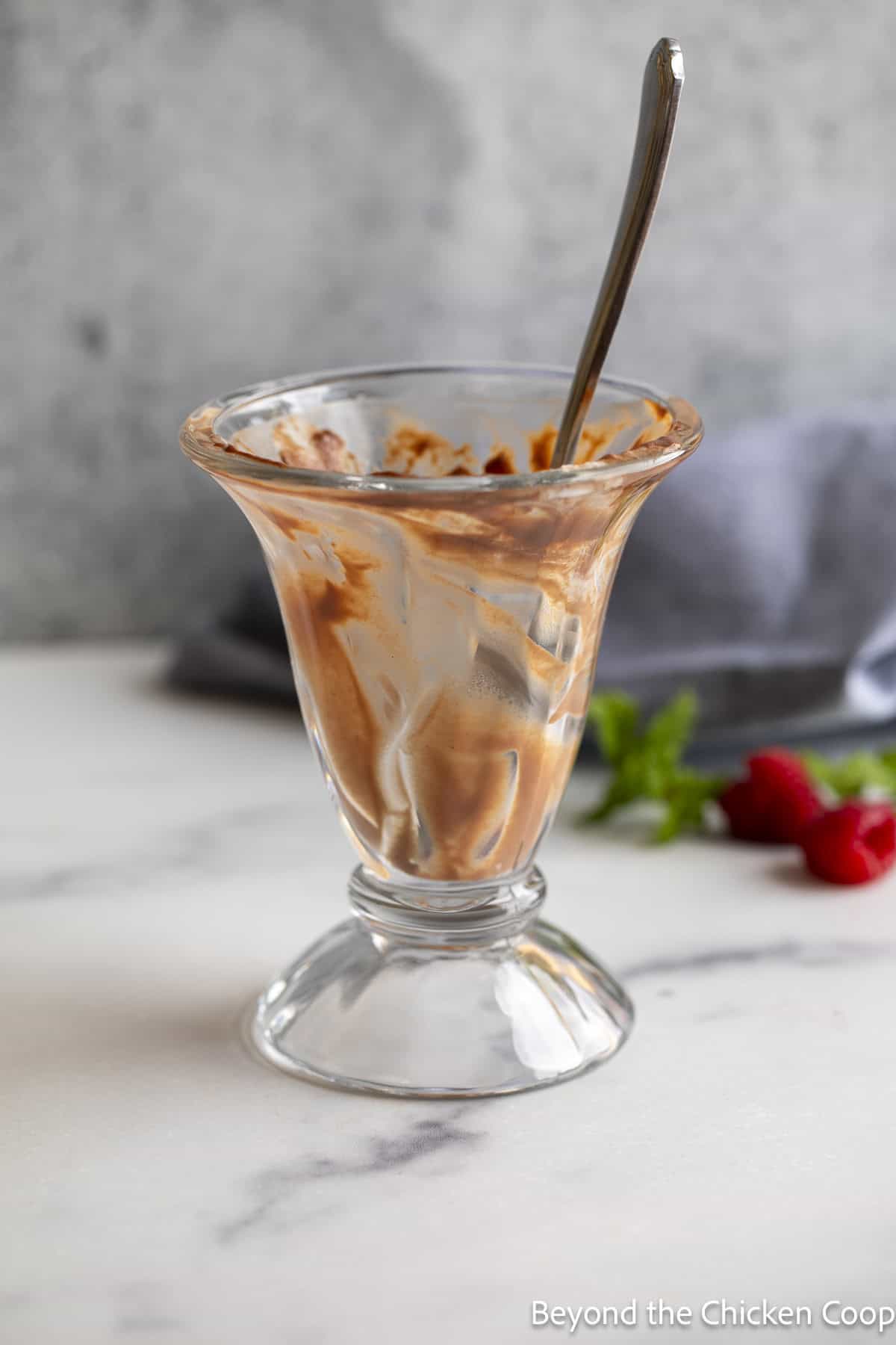 An empty glass with a bit of pudding and a spoon. 