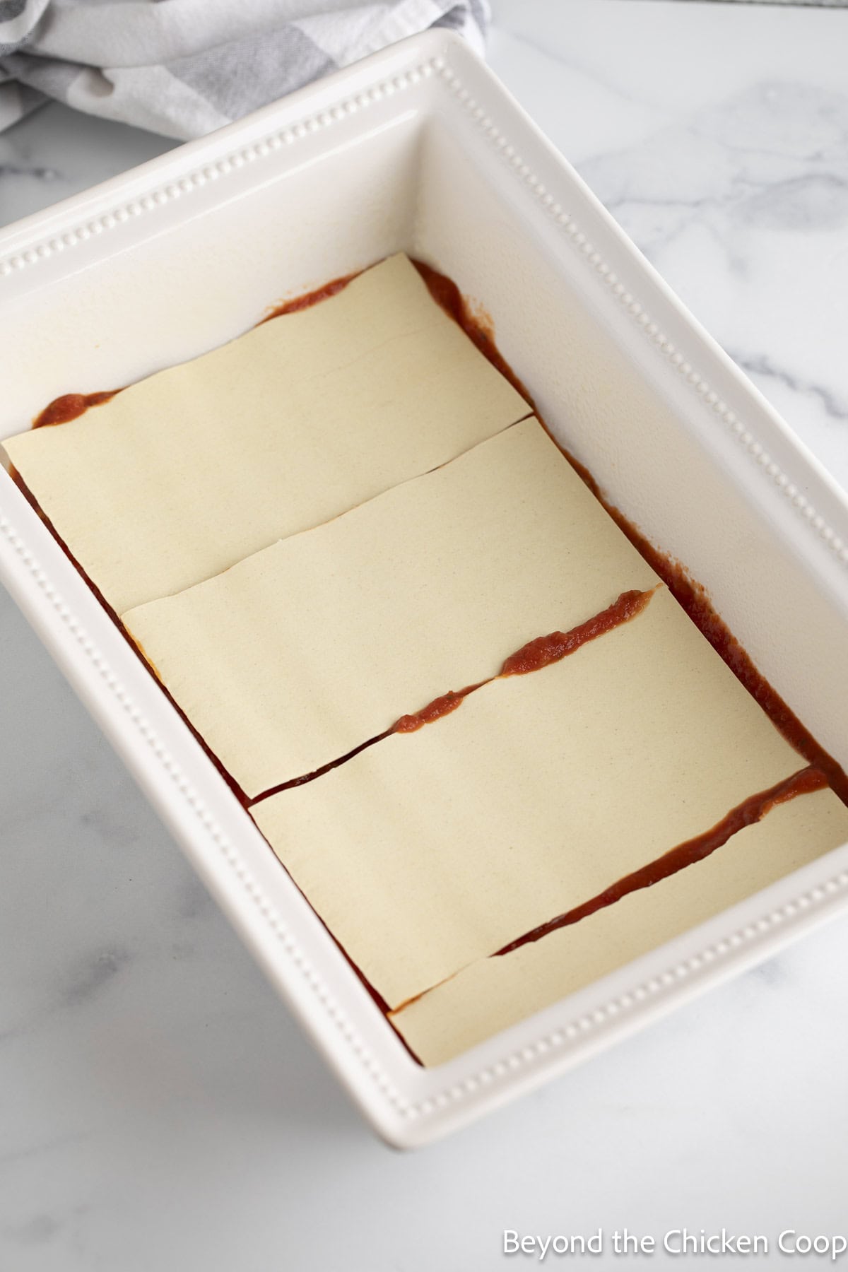 Layering a lasagna in a white casserole dish. 