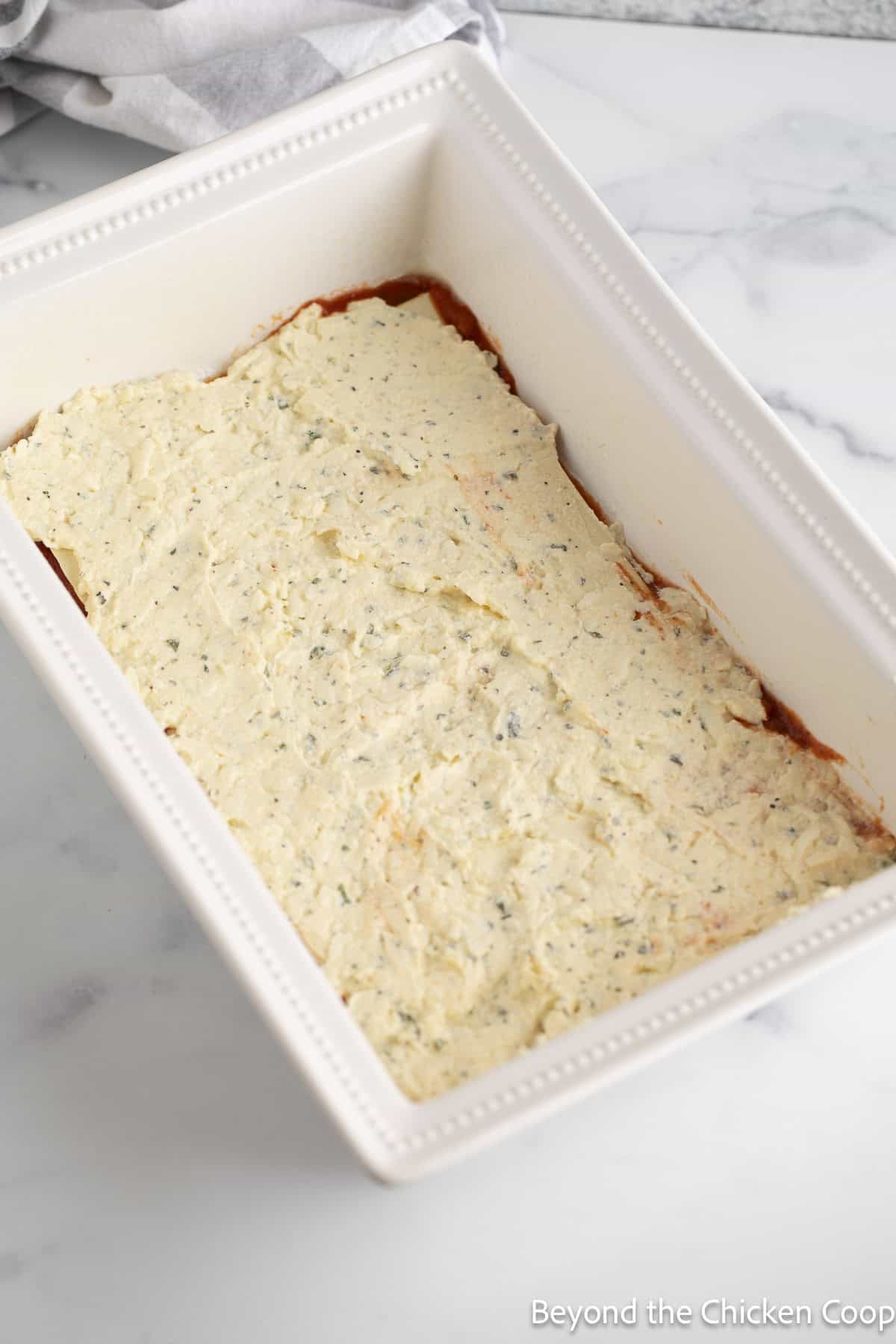 Adding the cheese layer to a homemade lasagna. 