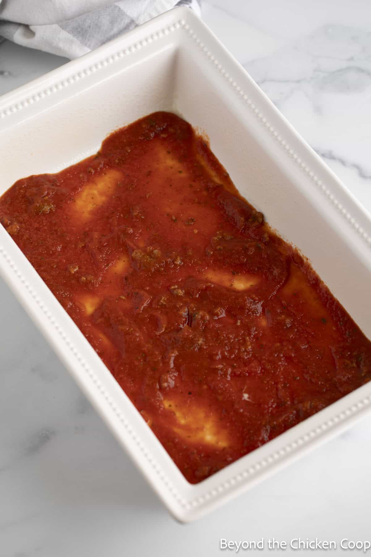 Marinara sauce in the bottom of a casserole dish. 