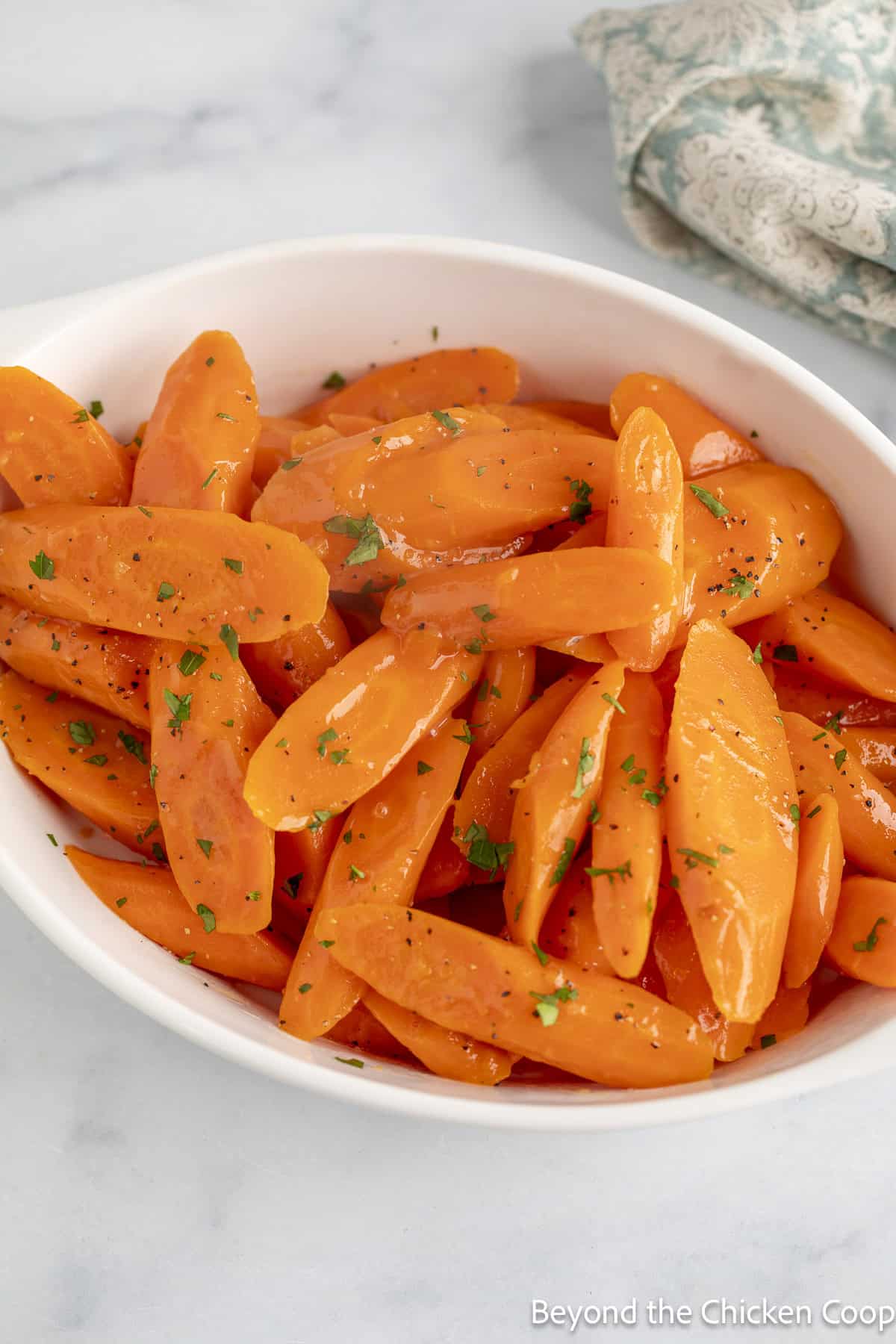 Cooked carrots topped with parsley in a white serving dish.