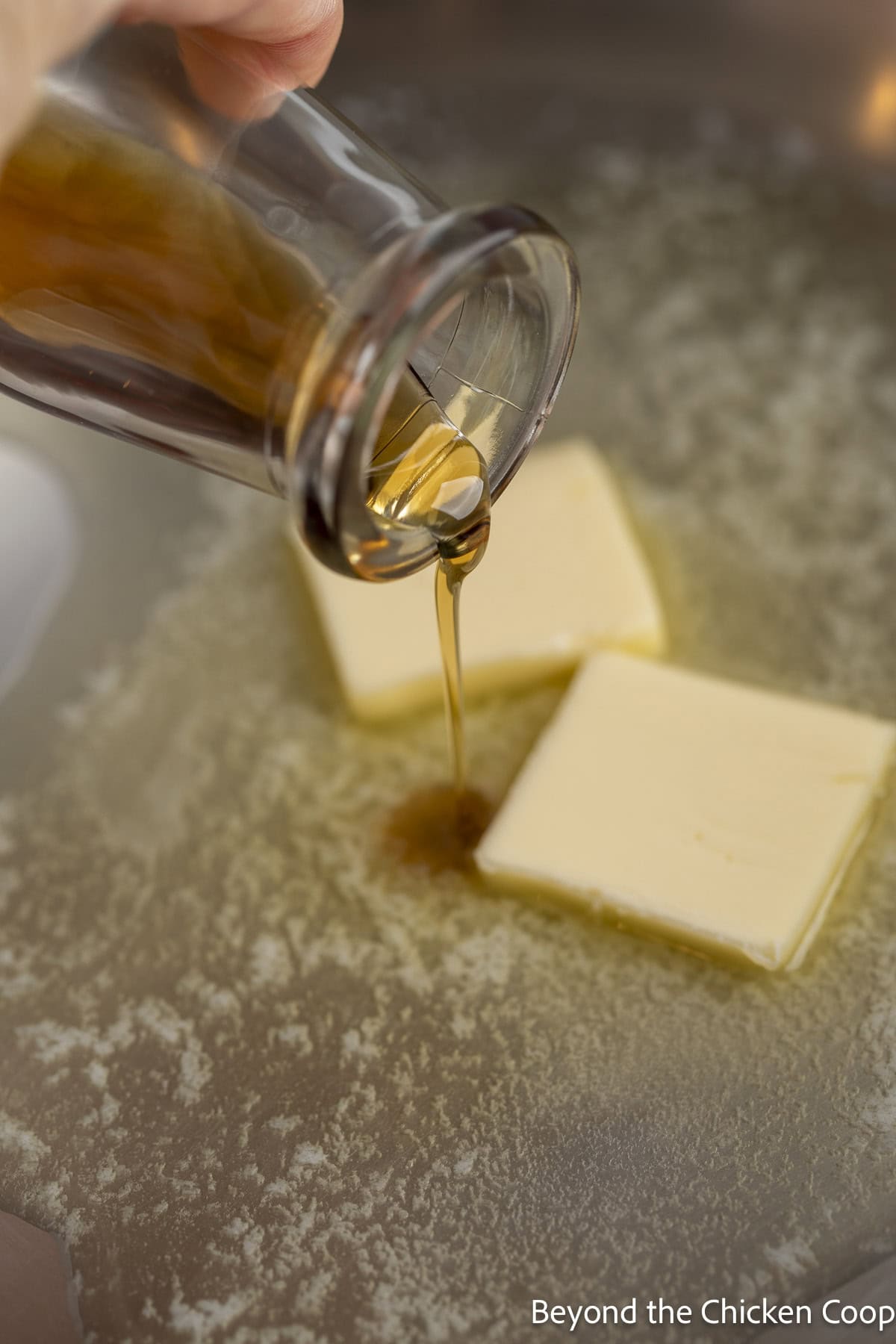 Maple syrup being poured into a saucepan with melted butter.