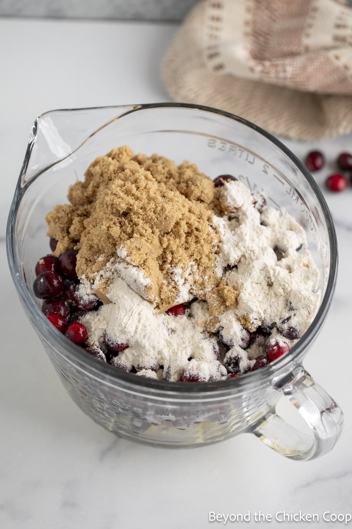 A large glass bowl filled with cranberries, apples, brown sugar, and flour.