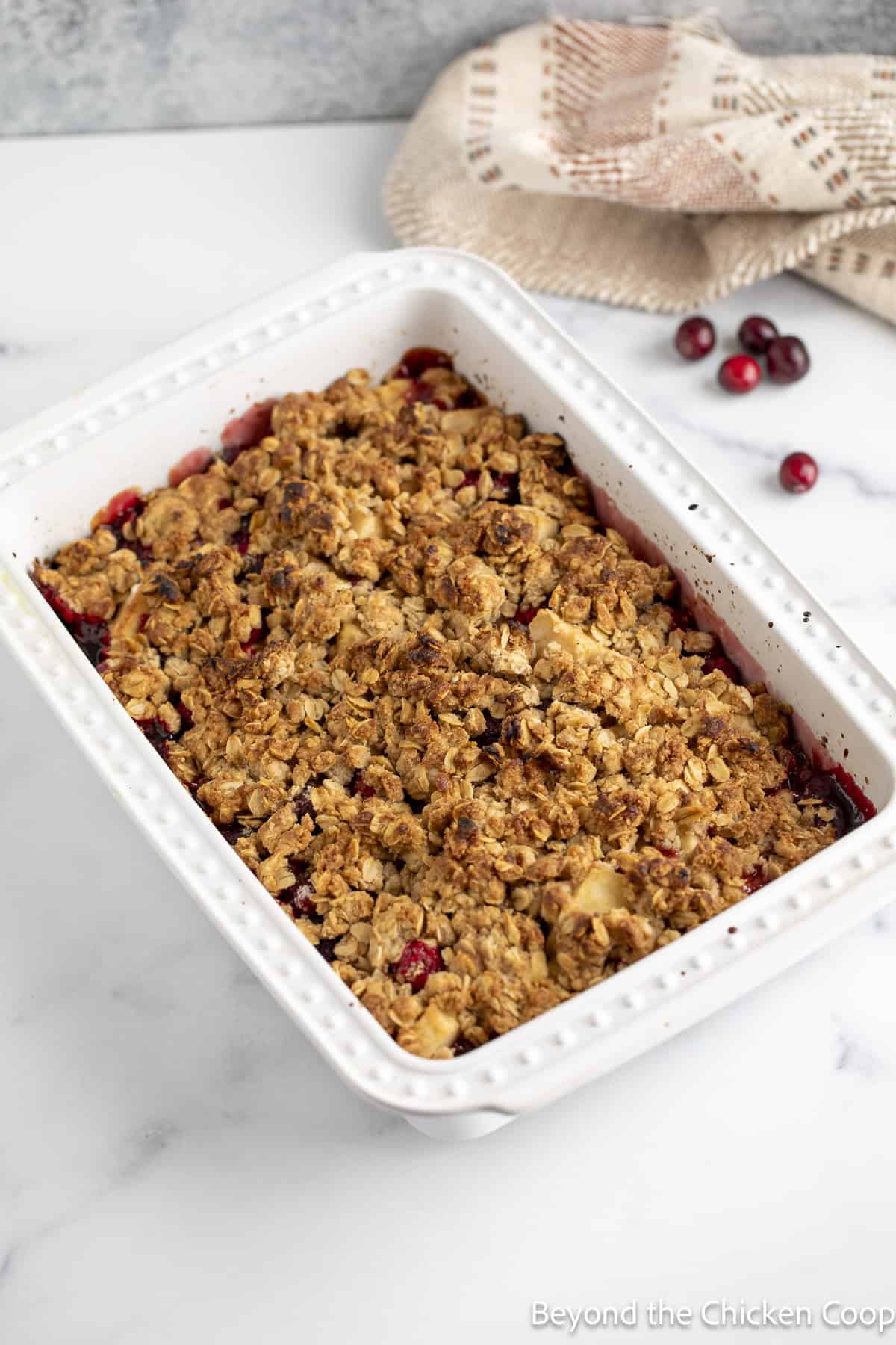 A baked apple crisp with cranberries in a white dish.