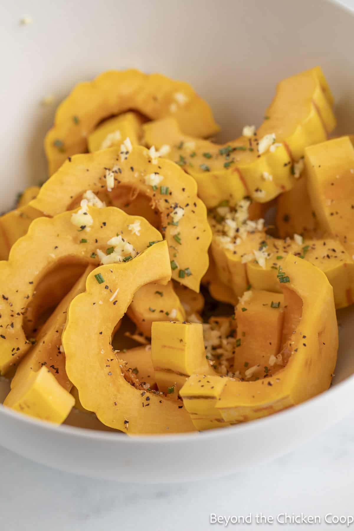 Sliced squash in a bowl tossed with olive oil, herbs, and garlic.