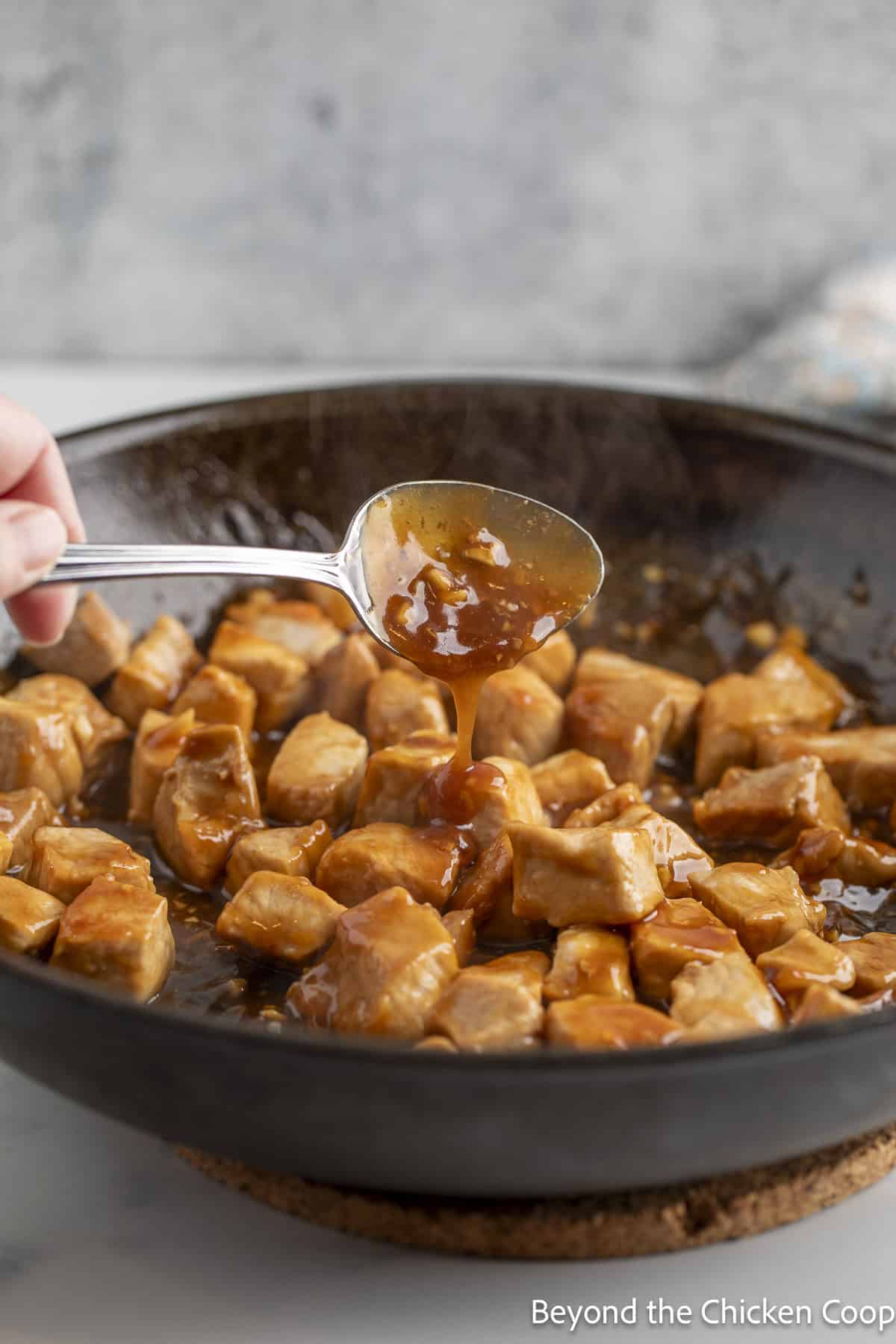 Thickened sauce pouring off a spoon onto pork in a pan.