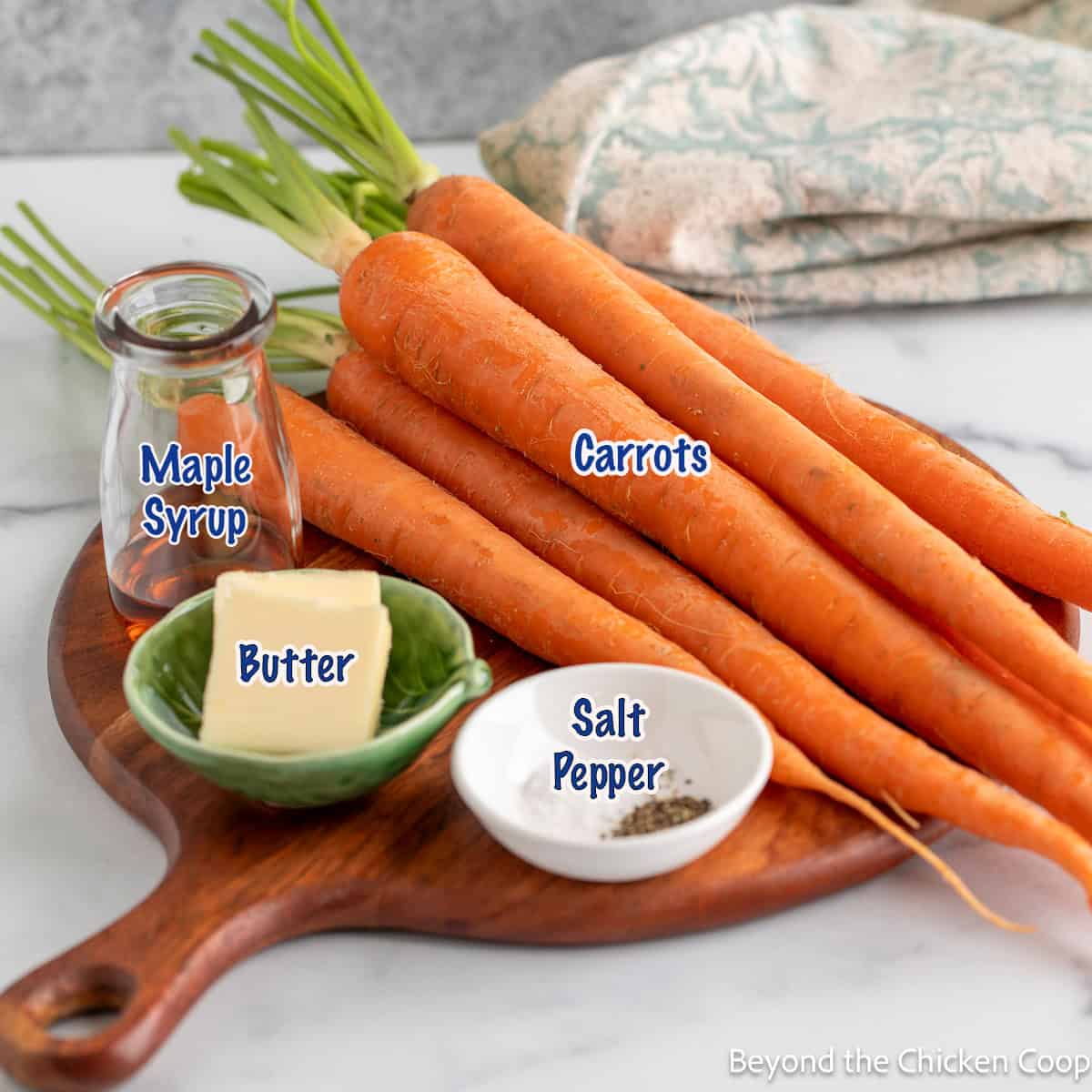 Fresh whole carrots on a wooden board, along with butter and maple syrup.