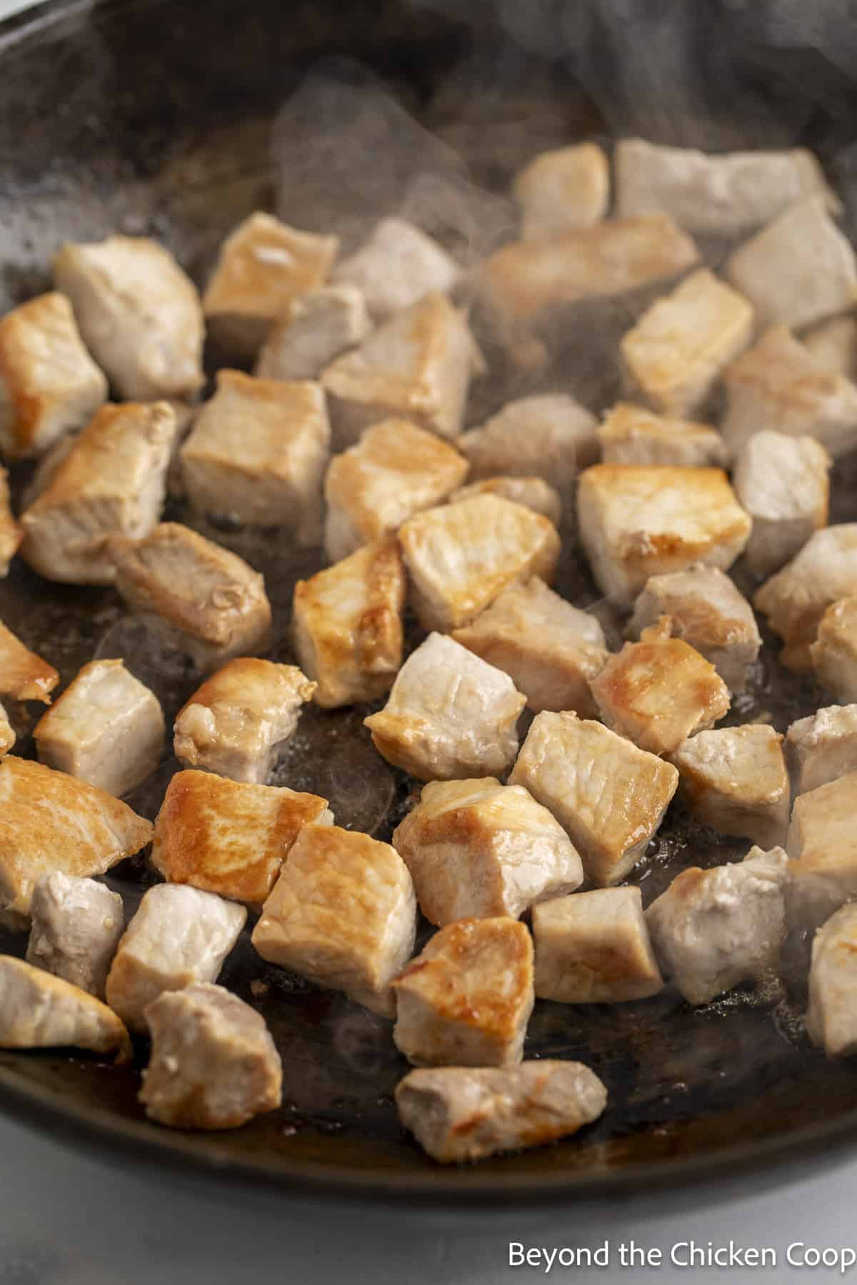Cooking small cuts of pork in a pan.
