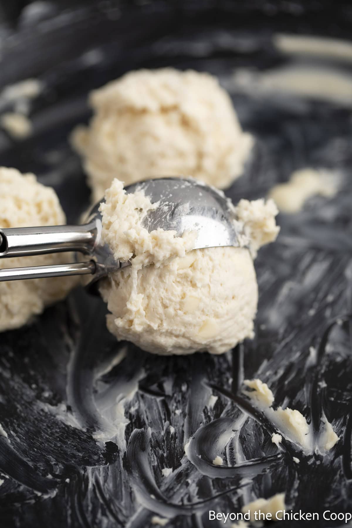 Using a scoop to drop dough in to a cast iron skillet.