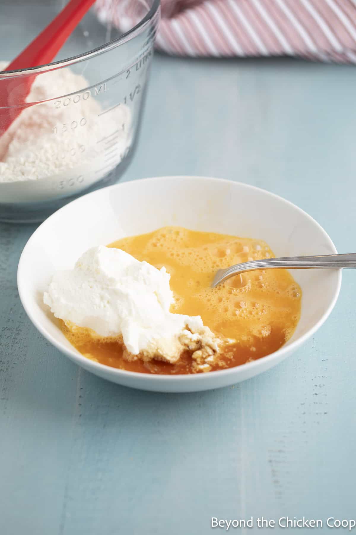A bowl with beaten eggs, yogurt, and vanilla.
