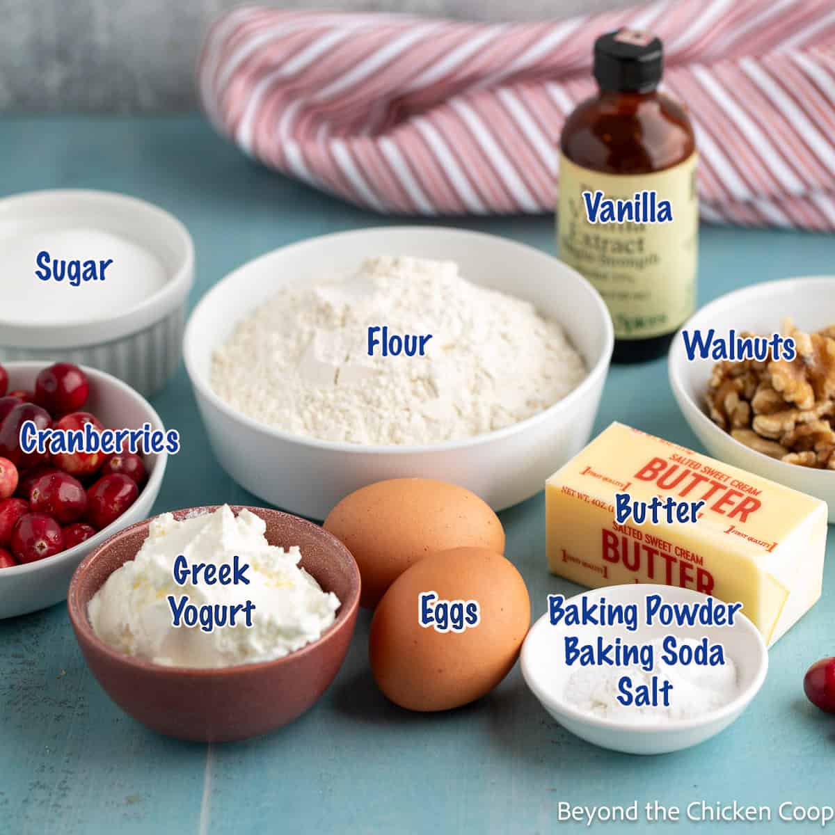 Bowls filled with flour, cranberries, walnuts, and sugar next to butter and eggs.