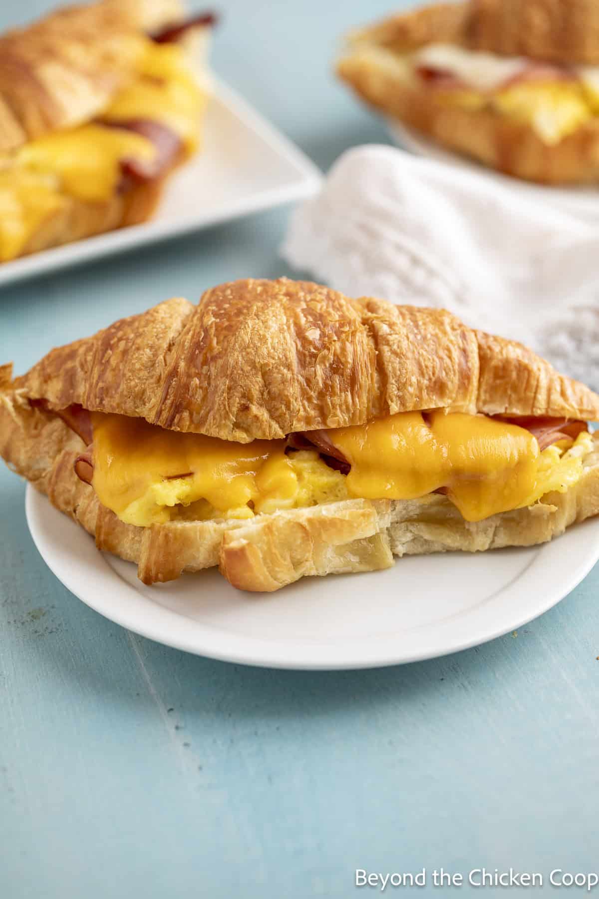 A croissant filled with eggs, ham and cheese on a white plate.