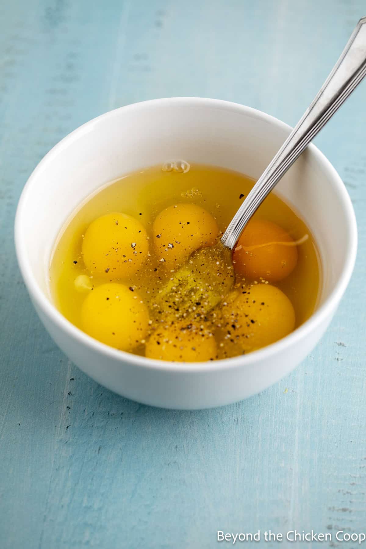 A white bowl filled with raw eggs and a fork.